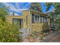 Charming yellow home featuring a white picket fence, siding, and black shuttered windows, nestled under a bright blue sky at 1665 S Madison St, Denver, CO 80210