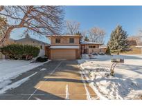 Inviting two-story house featuring a well-kept lawn, mature trees, and a paved driveway in a snow-covered landscape at 7318 W Cedar Cir, Lakewood, CO 80226