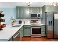 Well-lit kitchen with modern stainless steel appliances, light countertops, and sage-colored cabinetry at 15104 E Utah Pl, Aurora, CO 80012