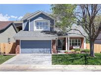 Charming two-story home featuring a gray garage door, blue siding, brick accents, and a well-manicured lawn at 13777 W Amherst Way, Lakewood, CO 80228