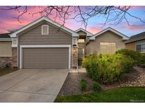 Charming home featuring a two-car garage, stone accents and manicured landscaping at sunset at 22312 E Plymouth Cir, Aurora, CO 80016
