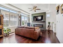 Cozy living room with fireplace, large windows, ceiling fan, and dark wood floors at 10560 Waco St, Commerce City, CO 80022