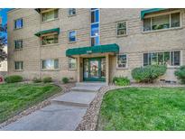 Inviting brick building entrance with green awning, glass door, and well-manicured lawn at 2100 N Franklin St # 15, Denver, CO 80205