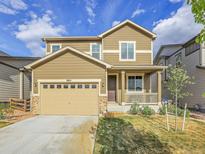 Two-story home with tan siding, a two-car garage, and a charming front porch at 9844 Truckee St, Commerce City, CO 80022