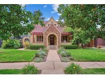 Charming brick home with a red-tiled roof, a manicured front lawn, and mature trees at 583 S York St, Denver, CO 80209