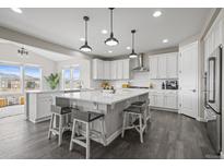 Bright kitchen features a large center island, white cabinetry, pendant lighting, and stainless steel appliances at 9021 Swan River St, Littleton, CO 80125