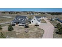 Expansive horse property featuring a light gray home with white trim, a covered porch, paddocks, and stables at 1465 Arabian Trl, Elizabeth, CO 80107