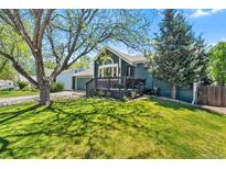 Inviting blue home with a charming front porch and lush green lawn under the shade of mature trees, creating a welcoming curb appeal at 8370 W Evans Pl, Lakewood, CO 80227