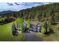Secluded gray home nestled among mature trees on a sprawling green lawn and with a mountain view at 2191 Baldy Ln, Evergreen, CO 80439