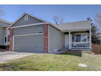 Charming home featuring a gray exterior, brick accents, a well-manicured lawn, and a cozy covered porch at 9659 Autumnwood Pl, Highlands Ranch, CO 80129