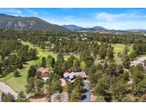 Stunning aerial view of mountain home nestled among mature trees and adjacent to a golf course at 2851 Interlocken Dr, Evergreen, CO 80439