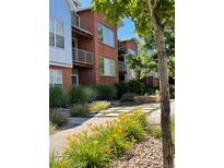 Modern brick townhome with metal accents, balcony, and landscaped walkway with yellow flowers at 85 Uinta Way # 405, Denver, CO 80230