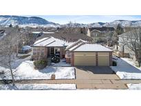 Tan two-story house with attached two-car garage, snowy yard, and mountain views at 17364 W 63Rd Dr, Arvada, CO 80403