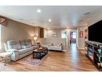 Inviting living room featuring a comfortable gray sofa, wood floors, and lots of natural light at 13871 Ivy St, Thornton, CO 80602