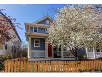 Charming two-story home featuring a bright red door and a lovely, fenced front yard with a flowering tree at 3353 Wabash St, Denver, CO 80238
