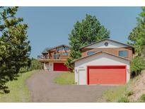 Inviting log cabin exterior with a red garage door and a charming mountain setting at 12135 Cochise Cir, Conifer, CO 80433