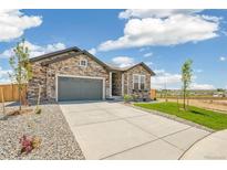 Charming stone-accented home with a gray garage door, complemented by a well-manicured lawn and landscaping at 6384 E 154Th Pl, Thornton, CO 80602