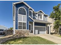 Charming two-story home boasts blue siding, stone accents, a manicured lawn, and an attached two-car garage at 9832 Kenton Cir, Commerce City, CO 80022