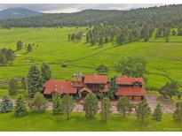 Stunning aerial view of a sprawling property with lush green fields and a charming home with a red roof at 5939 Lone Peak Dr, Evergreen, CO 80439