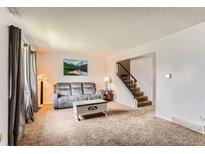 Bright living room featuring neutral carpet, gray couch, and stairs to the upper level at 8613 Santa Fe Dr, Thornton, CO 80260