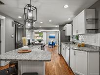 Bright kitchen with granite countertops, white cabinets, stainless appliances, hardwood flooring, and modern pendant lighting at 6943 Oak Way, Arvada, CO 80004