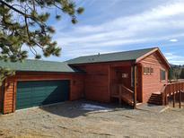 Charming red home featuring a green roof, matching green garage door, and rock landscaping at 656 County Road 72, Bailey, CO 80421