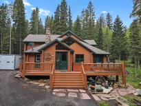 Charming log cabin featuring a spacious deck and hot tub surrounded by mature trees at 8905 Carol Ln, Conifer, CO 80433