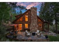 Charming log cabin with stone chimney and outdoor stone patio seating area at 80 Spruce Ct, Evergreen, CO 80439