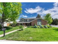 Inviting two-story home boasts a lush lawn, mature tree, and a charming brick and gray exterior at 10289 E Berry Dr, Greenwood Village, CO 80111