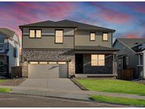 Two-story home with a stone facade, gray siding, and well-maintained lawn at sunset at 6156 Hourglass Dr, Brighton, CO 80601