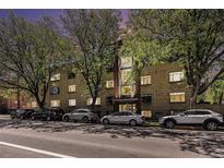 An exterior view of a multi-unit residential building on a tree-lined street with many parked cars at 500 E 11Th Ave # 102, Denver, CO 80203
