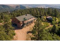 Stunning log home featuring an outdoor deck and a two-car garage nestled amid lush green trees and mountain scenery at 2518 N State Highway 67, Sedalia, CO 80135