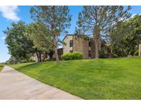 A charming exterior featuring a well-manicured lawn, lush trees, and a stone facade that adds architectural interest at 7740 W 87Th Dr # A, Arvada, CO 80005