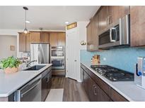 Modern kitchen featuring stainless steel appliances, wood cabinets, and a stylish blue tile backsplash at 7410 S Old Hammer Way, Aurora, CO 80016