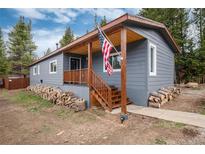Charming single-story home with a covered porch, wood piles, and an American flag at 192 Little Creek Rd, Idaho Springs, CO 80452