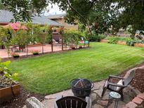 Spacious backyard featuring lush lawn, deck with seating, garden beds, and a cozy fire pit area at 6664 Gray St, Arvada, CO 80003
