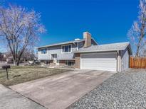 Split-level home featuring a two-car garage and a brick chimney on a sunny day at 7449 W Fremont Ave, Littleton, CO 80128