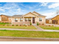 Charming ranch style home with tan siding, stone accents, landscaped yard, and covered porch at 10771 N Montane Dr, Broomfield, CO 80021