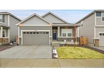 Charming single-Gathering home showcasing gray siding, stone accents, a well-manicured lawn, and an attached two-car garage at 239 Chipeta Way, Lochbuie, CO 80603