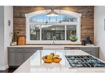 Bright kitchen featuring an island with a cooktop, gray cabinets, quartz counters, and wood-paneled backsplash at 3039 N Milwaukee St, Denver, CO 80205