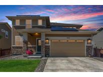 Beautiful two-story home featuring a two car garage, manicured lawn, and stylish stone accents under a colorful sunset sky at 1933 Griffin Dr, Brighton, CO 80601