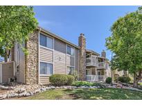 Beautiful condo exterior featuring stone accents, wood siding, a well-manicured lawn, and mature trees at 4400 S Quebec St # D203, Denver, CO 80237