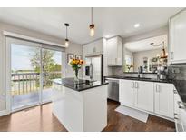 Bright white kitchen with black countertops, stainless appliances, and a door leading to an outdoor deck at 19131 E Garden Pl, Centennial, CO 80015