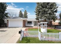 Charming brick ranch home with a well-manicured lawn, white picket fence, and mature trees at 3089 S Quintero Way, Aurora, CO 80013