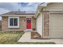 Charming single-story home featuring a brick facade, attached two-car garage, a red door, and solar panels at 5587 S Simms Way, Littleton, CO 80127