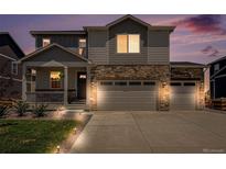 Charming two-story home features a stone facade, three-car garage, and a welcoming front porch at twilight at 7415 E 158Th Pl, Thornton, CO 80602