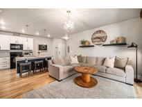 Open-concept living room featuring hardwood floors, a modern chandelier, and a large, comfortable sectional sofa at 15274 W 64Th Ln # 206, Arvada, CO 80007