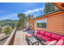A spacious log home with an inviting deck featuring red outdoor furniture, perfect for enjoying mountain views at 22349 Natsihi Rd, Indian Hills, CO 80454