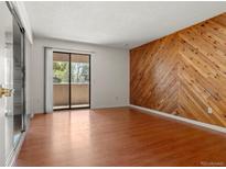 Bright living room boasts sleek hardwood floors, a private balcony, and an accent wall with herringbone wooden panelling at 3662 S Granby Way # J05, Aurora, CO 80014