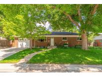 Charming brick home featuring mature trees, lush green lawn, and inviting curb appeal at 1410 S Ammons St, Lakewood, CO 80232